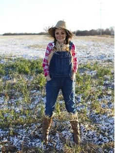 a woman wearing overalls and cowboy boots standing in a field with snow on the ground