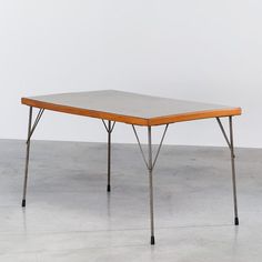 a rectangular table with two legs and a wooden top on the floor in front of a white wall