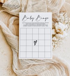 a baby shower game on top of a table next to some white flowers and leaves