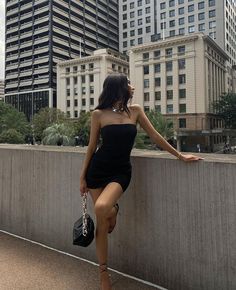 a woman leaning on a wall in front of some tall buildings with her legs spread out