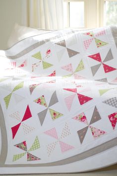 a quilted bed with white sheets and pink and green triangles on the bedspread