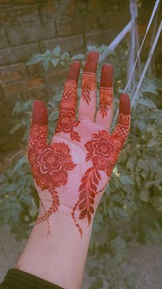 a person's hand with red henna and flowers painted on it, in front of some bushes