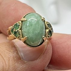 This vintage ring is a unique piece of fine jewelry crafted with 14k yellow gold. The main stone is a natural cabochon jade in a beautiful shade of green, complemented with seven emerald gemstones. The ring is a size 7 and has a cocktail style, perfect for any occasion. The brand of this ring is Thiland and it is a truly exquisite piece to add to any jewelry collection. Jade Engagement Ring, Emerald Gemstone, Dream Jewelry, Vintage Ring, Emerald Ring, Shades Of Green, Vintage Rings, Jewelry Crafts, Unique Pieces