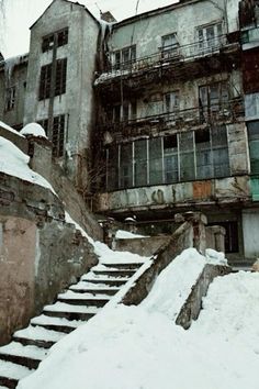 an old run down building with snow on the ground and stairs leading up to it