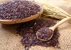 a wooden spoon filled with purple rice next to stalks of oats on a sack