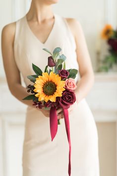 a woman in a white dress holding a sunflower bouquet