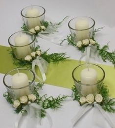 four glass vases with white roses and greenery are arranged on a yellow ribbon