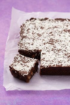 chocolate cake with coconut on top cut into squares and placed on wax paper over purple background