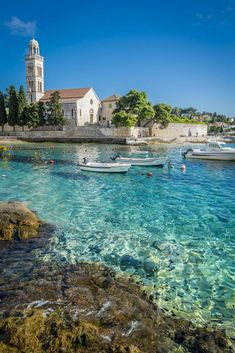 people swimming in clear blue water next to a white church and small boats on the shore