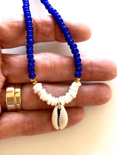 Beaded shell choker with cobalt blue African glass beads, Hawaiian white puka shells, genuine cowrie shell and Karen Hill Tribe 24k gold vermeil accents. Beaded summery necklace features vintage cobalt blue African white heart trade beads and genuine sea shells. Little white Hawaiian puka shells and genuine cowrie shell focal. Karen Hill Tribe 24k gold vermeil cube beads add fabulous accents. Beaded necklace closes with 14k gold fill spring ring clasp and findings. Handmade Blue Shell Beaded Necklaces, Vacation Shell Jewelry In Blue, Handmade Blue Shell, Blue Shell Necklace For Vacation, Blue Beaded Shell Strand Necklace, Blue Shell-shaped Jewelry For Vacation, Blue Shell Beaded Bracelet As Gift, Blue Shell Beaded Bracelet For Gift, Blue Shell Beaded Bracelets For Gift