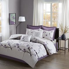 a bed with purple and white comforters in a room next to a window,