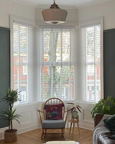 a living room filled with furniture and windows covered in white shuttered shades on either side of the window