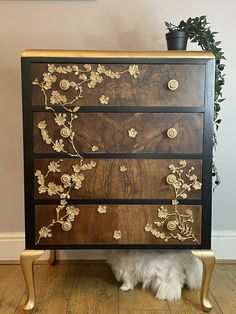 a dog sitting under a dresser with flowers painted on the drawers and gold trimmings