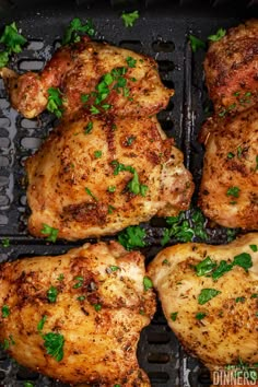 four pieces of chicken sitting on top of a grill with parsley sprigs