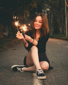 a woman sitting on the road holding sparklers