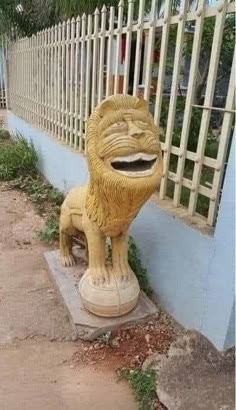 a statue of a lion sitting on top of a cement block next to a fence