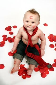 a baby wearing a red tie and sitting on the ground with petals scattered around it