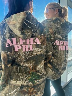 two women wearing camouflage jackets with pink letters on them