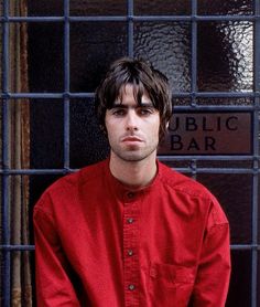 a man in a red shirt leaning against a wall