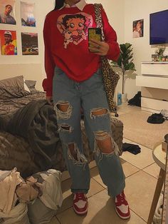 a woman standing in front of a bed wearing ripped jeans and a red shirt with an animal print on it