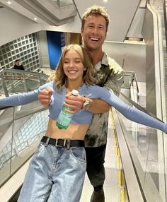 a man and woman walking down an escalator with their arms around each other