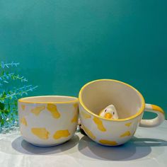 two yellow and white cups sitting next to each other on a table with blue flowers in the background