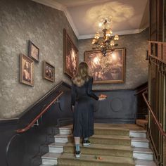 a woman is walking down the stairs in an old fashioned house with paintings on the walls