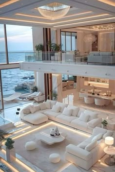 a living room filled with white furniture and lots of windows next to the ocean at night