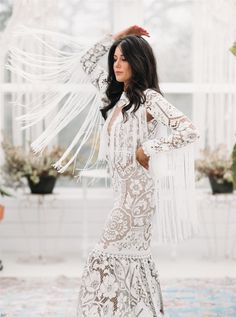 a woman in a long white dress with feathers on her head and hands behind her head