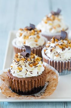 three cupcakes with white frosting and chocolate toppings on a square plate