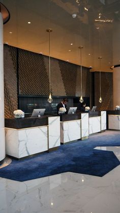 an office lobby with marble counter tops and blue carpeted flooring, along with chandeliers hanging from the ceiling