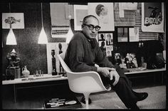 black and white photograph of man sitting in chair with art on the wall behind him