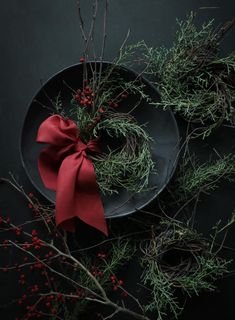 a black plate with a red bow on top of it next to branches and berries