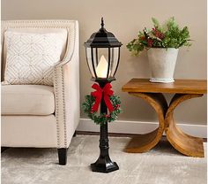 a lamp post with a christmas wreath on it next to a chair and potted plant