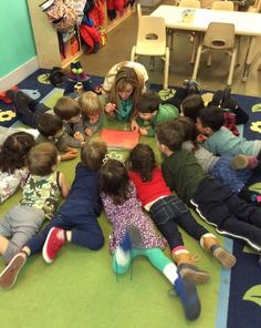 a group of children sitting on the floor in a circle playing with an open book