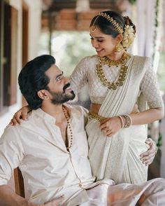 a man sitting next to a woman in a white sari on top of a bed