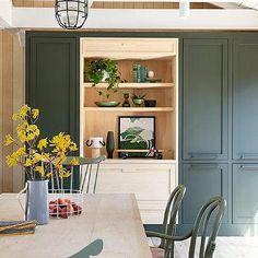 a dining room table with chairs and vases on top of it in front of green cupboards