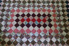 an old quilt is laying on top of a tablecloth that has many different colors and patterns