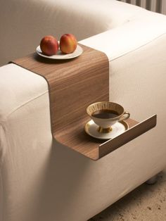 a coffee cup and saucer sitting on a table next to a white couch with two apples