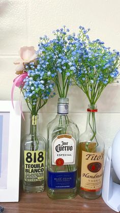 three bottles with flowers in them sitting on a shelf next to a framed photograph and an empty bottle