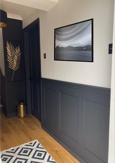 an empty room with wood floors and gray paneling, framed art on the wall