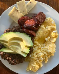 a white plate topped with eggs, sausage and other breakfast foods on top of a wooden table