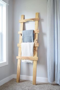 a wooden ladder with towels on it in front of a white wall and window, next to a carpeted floor