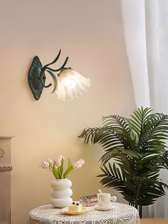 a table with two vases on it next to a potted plant and lamp