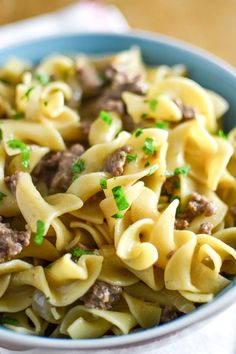 a blue bowl filled with pasta and meat on top of a table next to a fork