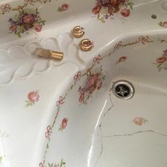 a sink that has some gold handles on it's faucet and is decorated with pink flowers