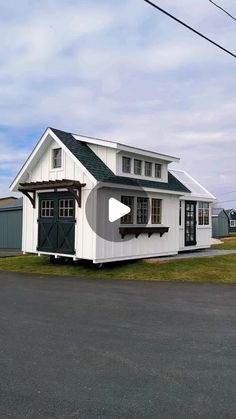 a small white house sitting on the side of a road next to a green field