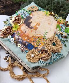 an altered purse is sitting on a table with flowers and chains attached to the bag