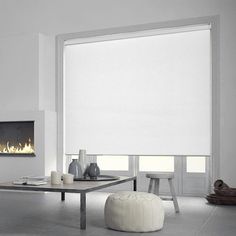 a modern living room with white walls and furniture, including a large window covered in roller shades