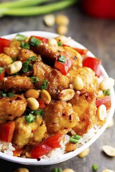 a white bowl filled with chicken and vegetables on top of rice covered in cashews